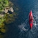 A person in a kayak paddling alongside a rocky shore full of lush greenery